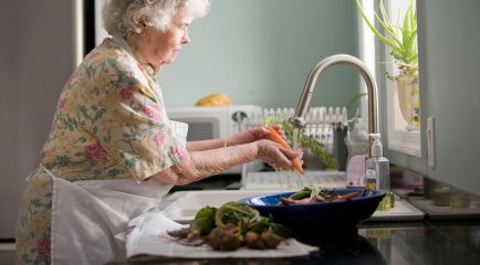 Eldre kvinne vasker grønnsaker i kjøkkenvask